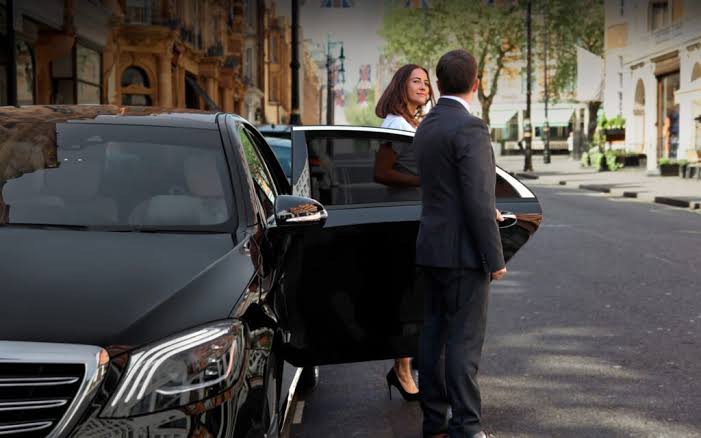 Chauffeur ouvrant la porte d'une berline de prestige à une cliente